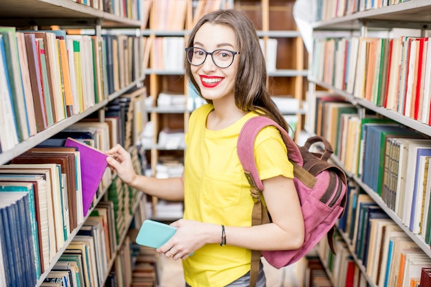 Młoda szczęśliwa i entuzjastyczna studentka przeszukująca książki na półkach w bibliotece