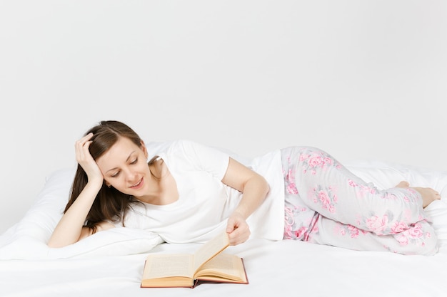 Młoda szczęśliwa kobieta leżąc w łóżku z białym prześcieradłem, poduszką, kocem na białej ścianie