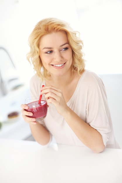 młoda szczęśliwa kobieta pijąca smoothie w kuchni