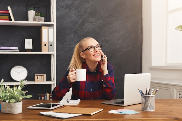 Młoda szczęśliwa kobieta rozmawia przez telefon i przerwę na kawę w nowoczesnym biurze, miejsce. Doradztwo biznesowe, prywatna rozmowa w pracy