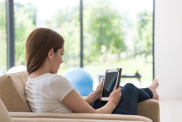 młoda szczęśliwa kobieta siedzi na kanapie z komputerem typu tablet w luksusowym domu