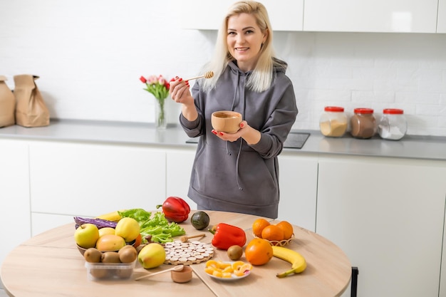 Młoda szczęśliwa kobieta trzyma miód korzystających podczas gotowania zdrowej żywności w kuchni. Dieta Detox, koncepcja żywienia utraty wagi.