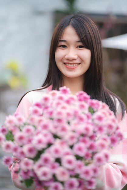 Młoda szczęśliwa kobieta uśmiechająca się z różowym kwiatem kwitnącym całkiem ładny portret dziewczyny latem z rośliną kwiatową natury w różowym kolorze i kolorowym naturalnym zewnątrz