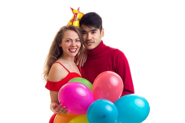 Młoda szczęśliwa kobieta w czerwonej sukience z kolorowym kapeluszem i przystojny mężczyzna w czerwonej koszuli dmuchający balony