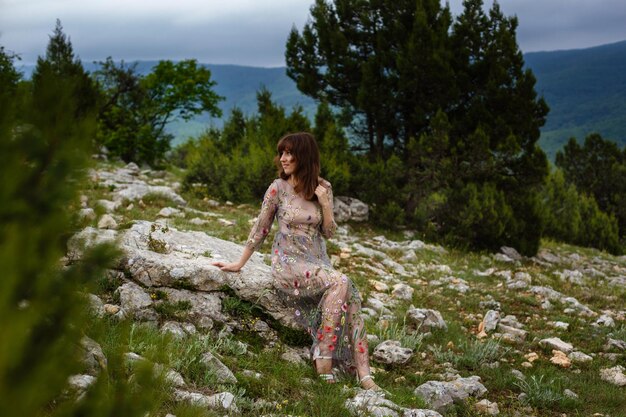 Młoda szczęśliwa kobieta w długiej sukni na zboczu góry Dziewczyna na łonie natury na tle błękitnego nieba Fotografia mody