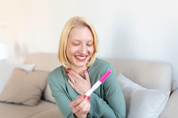 Młoda szczęśliwa kobieta z pozytywnym wynikiem testu ciążowego płytka głębia ostrości Szczęśliwa, że będzie miała dziecko Wreszcie jest w ciąży