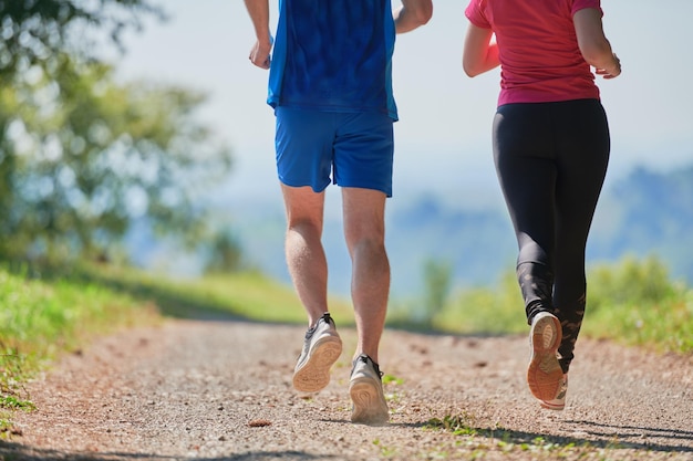 młoda szczęśliwa para ciesząca się zdrowym stylem życia podczas joggingu po wiejskiej drodze przez piękny słoneczny las, ćwiczenia i koncepcje fitness