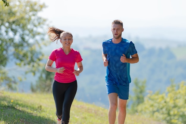 młoda szczęśliwa para ciesząca się zdrowym stylem życia podczas joggingu po wiejskiej drodze przez piękny słoneczny las, ćwiczenia i koncepcje fitness