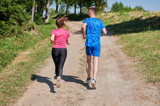 Zdjęcie młoda szczęśliwa para ciesząca się zdrowym stylem życia podczas joggingu po wiejskiej drodze przez piękny słoneczny las, ćwiczenia i koncepcje fitness