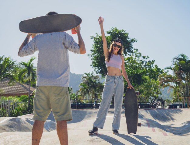 Młoda szczęśliwa para na deskorolkach bawi się longboardem w skateparku