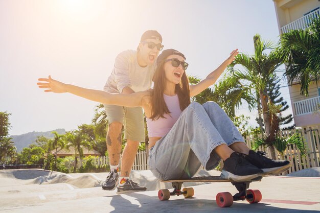 Młoda szczęśliwa para z deskorolkami lubi jeździć na longboardzie w skateparku