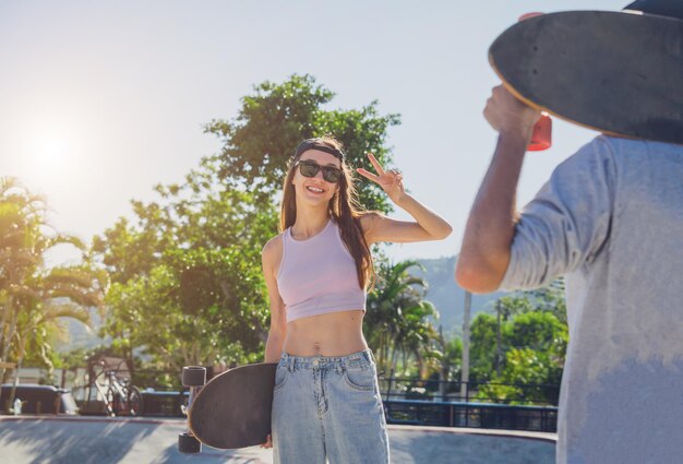 Młoda szczęśliwa para z deskorolkami lubi jeździć na longboardzie w skateparku