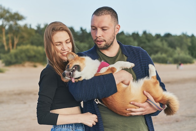 Młoda szczęśliwa para z psem stojącym na plaży. Życie rodzinne, bycie razem, mąż i żona relaksują się razem