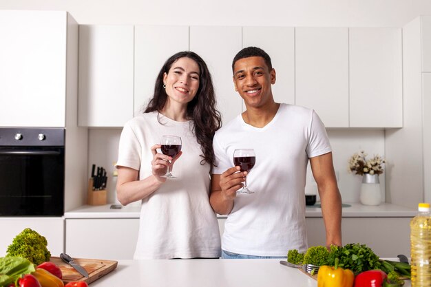 Młoda szczęśliwa para z wielu ras pije wino w białej nowoczesnej kuchni Afroamerykanin dzwoni kieliszki
