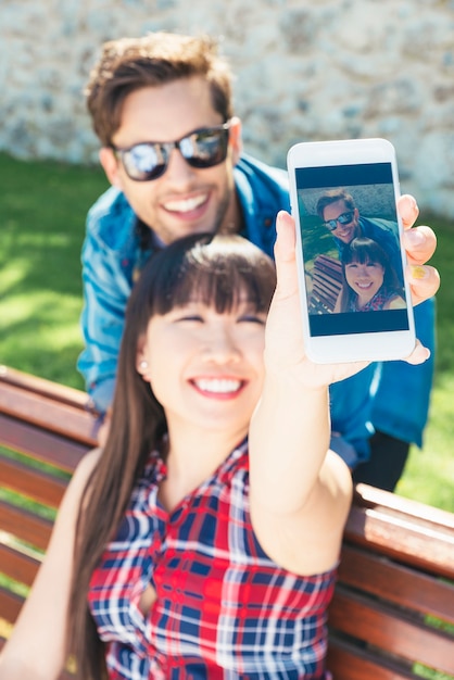 Młoda szczęśliwa para za pomocą smartfona siedzi w parku
