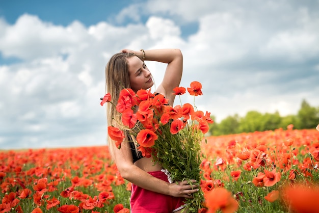 Młoda szczęśliwa ukraińska kobieta trzyma bukiet kwiatów maku, spacery i cieszyć się słonecznym dniem w polu