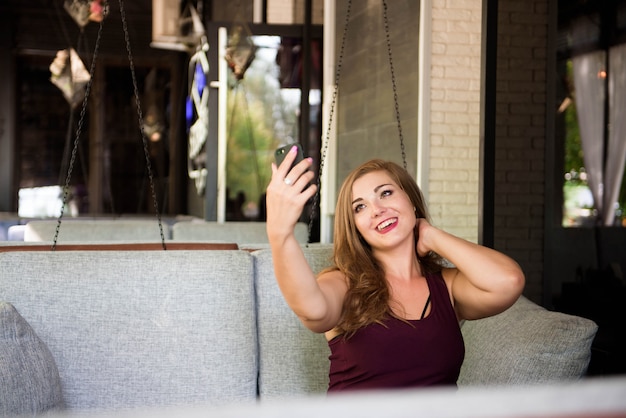 Młoda szczęśliwa uśmiechnięta piękna plus size model robi selfie, xxl kobieta w kawiarni.