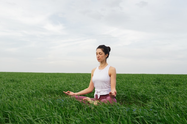Młoda szczupła dziewczyna robi joga na świeżym powietrzu w zielonym polu