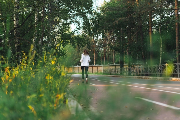 Młoda szczupła kobieta brunetka w strojach sportowych biegających w jesiennym parku w czasie wschodu słońca o złotej godzinie