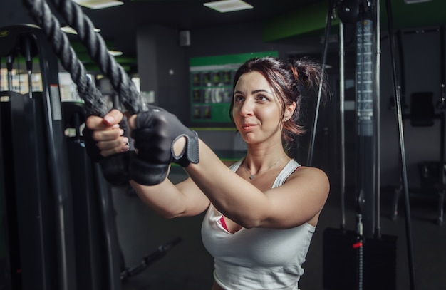 Młoda szczupła kobieta ćwiczy przedłużanie ramion z linami w maszynie do ćwiczeń na siłowni