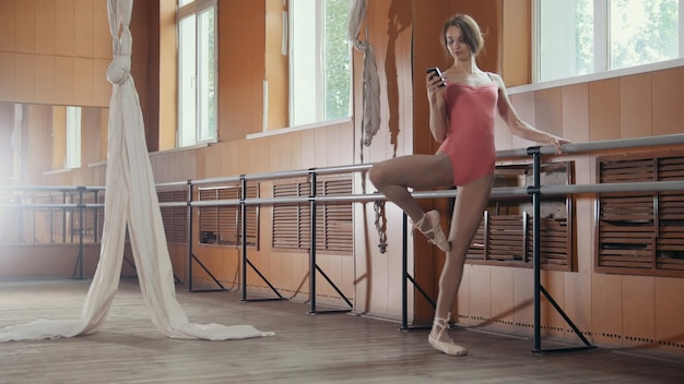 Zdjęcie młoda tancerka używa smartfona w sali baletowej, szeroki kąt