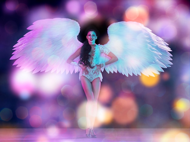 Młoda tancerka ze skrzydłami anioła w neonowym świetle na czarnym tle w latającym konfetti