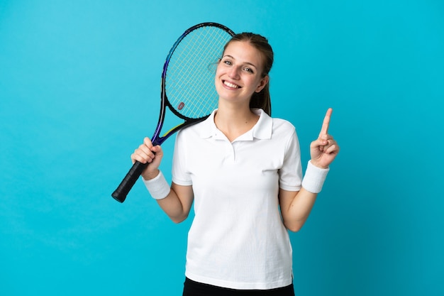 Młoda tenisistka kobieta na białym tle na niebieskiej ścianie pokazując i podnosząc palec na znak najlepszych