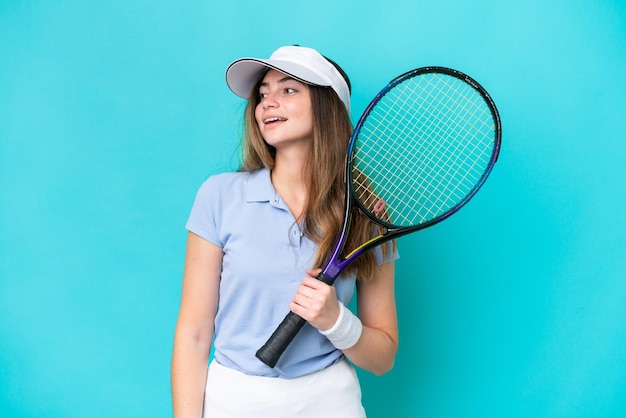 Młoda tenisistka na białym tle na niebieskim tle, patrząc w bok i uśmiechnięta