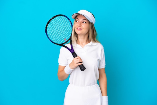 Młoda tenisistka rumuńska kobieta odizolowana na niebieskim tle, patrząc w bok i uśmiechnięta