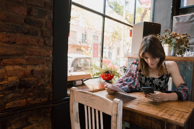 Młoda transseksualna Latynoska siedząca w restauracji za pomocą telefonu zamawiającego jedzenie