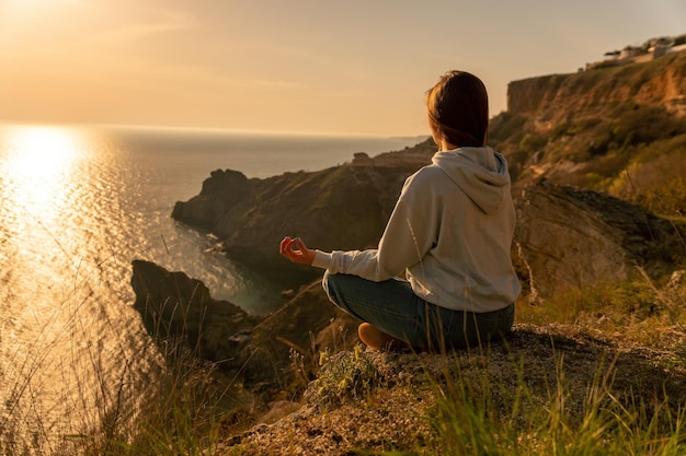 Młoda turystka, ciesząca się zachodem słońca nad morzem, górskim krajobrazem, siedząc na świeżym powietrzu damskiej jogi