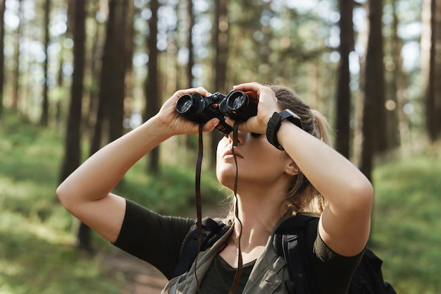 Młoda turystka używa lornetki do obserwacji ptaków w zielonym lesie