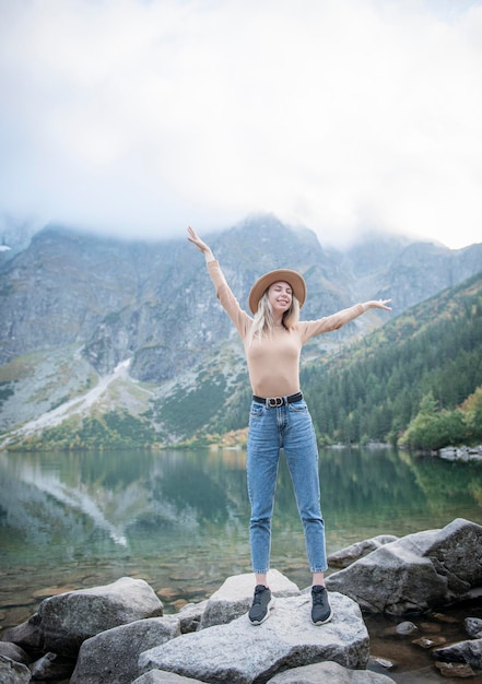 Młoda turystka w kapeluszu z rękami w górze na szczycie góry podziwia przyrodę