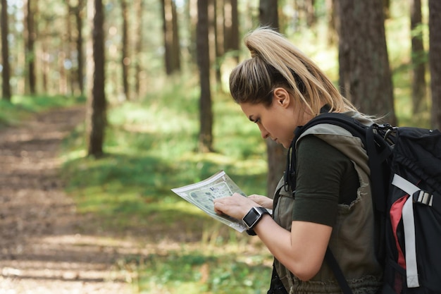 Młoda turystka z dużym plecakiem, korzystająca z mapy do biegów na orientację w lesie