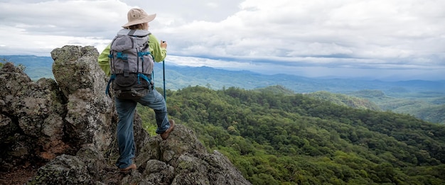 Młoda turystka z plecakiem relaksująca się na szczycie skały i podziwiająca widok na góry