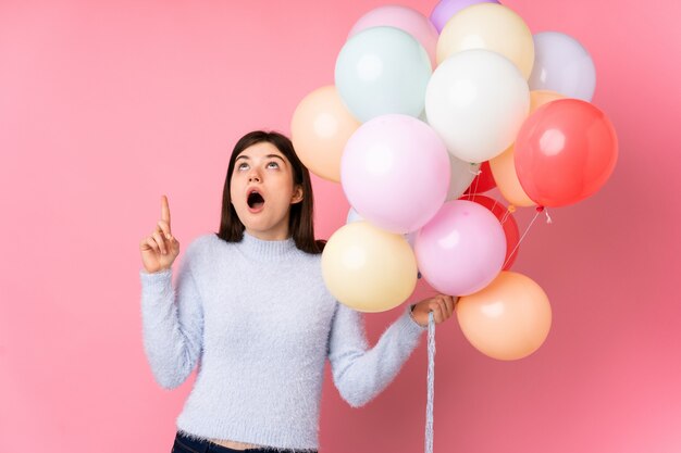 Młoda ukraińska nastolatka trzyma balony na różowej ścianie, wskazując palcem wskazującym, świetny pomysł