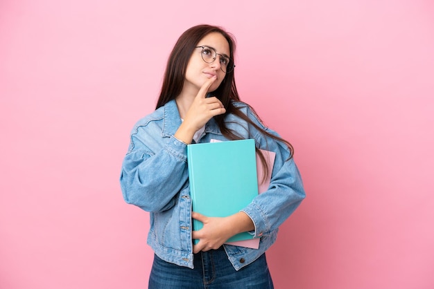 Młoda ukraińska studentka odizolowana na różowym tle, mająca wątpliwości podczas patrzenia w górę