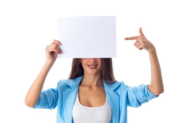 Młoda urocza kobieta w białej koszulce i niebieskiej kurtce, zakrywająca połowę twarzy białą kartką papieru