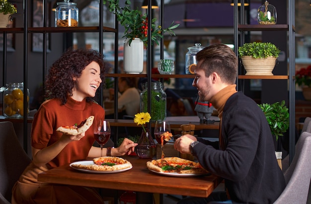 Młoda urocza para je pizzę w pizzerii. facet bawi swoją dziewczynę w restauracji. Szczęśliwi ludzie bawią się razem