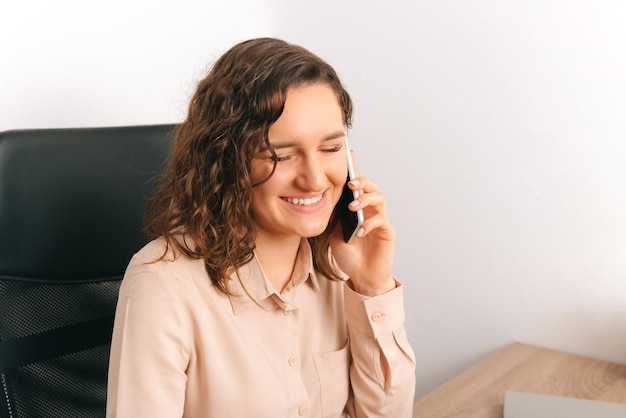 Młoda urocza śmiejąca się kobieta rozmawia przez telefon w biurze