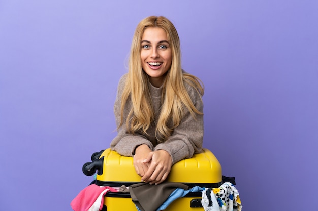 Młoda Urugwajska blondynki kobieta z walizką pełną ubrania nad odosobnioną purpury ścianą