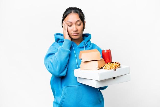 Młoda Urugwajska kobieta trzymająca pizze i hamburgery na białym tle z bólem głowy