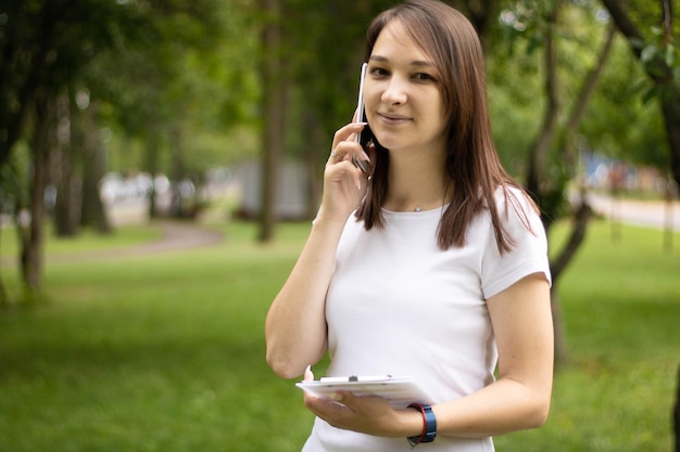 Młoda uśmiechnięta Azjatka rozmawiająca przez telefon komórkowy, stojąca w nowoczesnym biurze z dokumentem w niej