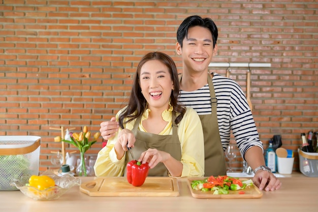 Młoda uśmiechnięta azjatycka para ubrana w fartuch w koncepcji gotowania w kuchni