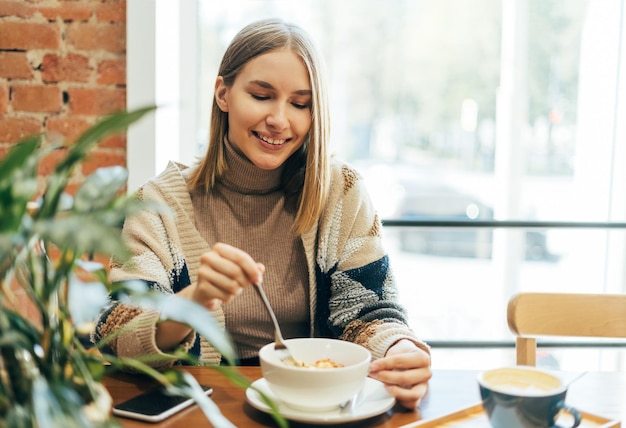 Młoda uśmiechnięta blondynka w swobodnym ubraniu jedząca lunch w kawiarni