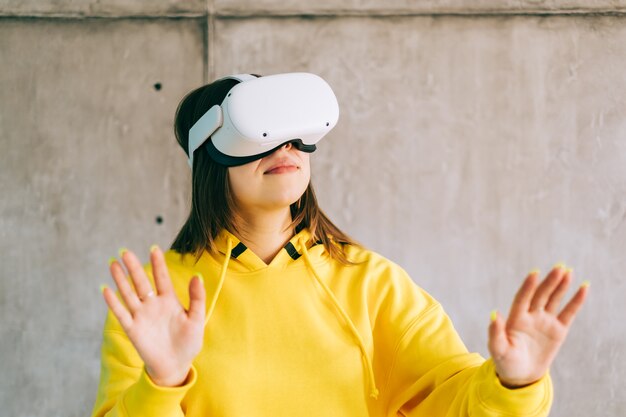 Młoda uśmiechnięta kaukaski kobieta za pomocą zestawu VR, gestykuluje i szuka w wirtualnej rzeczywistości.