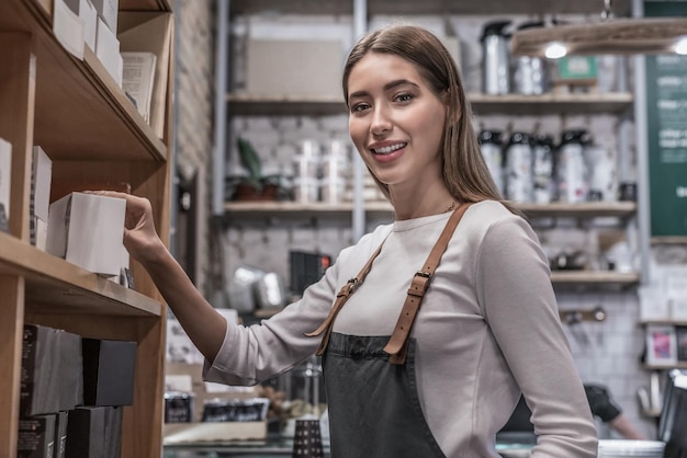 Młoda uśmiechnięta kobieta barista biorąca kawę w sklepie dla klienta