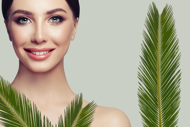 Młoda uśmiechnięta kobieta o czystej, świeżej skórze i zielonych liściach Zabieg na twarz i kosmetologia