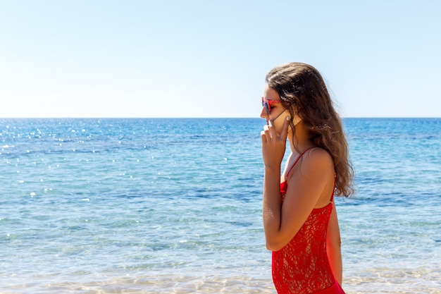 Młoda uśmiechnięta kobieta opowiada telefonem na plaży