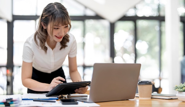 Młoda Uśmiechnięta Kobieta Pracuje Przy Laptopie I Cyfrowym Tablecie W Biurze Na Otwartej Przestrzeni